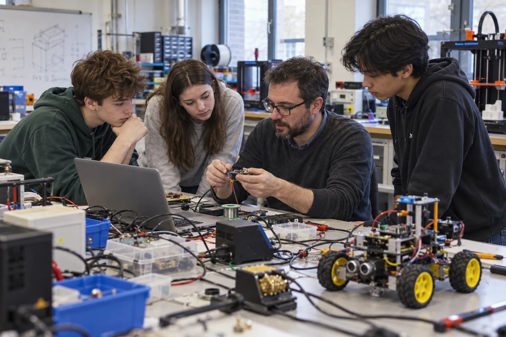Tres alumnos y un profesor montan un circuito junto a un pequeño robot con ruedas